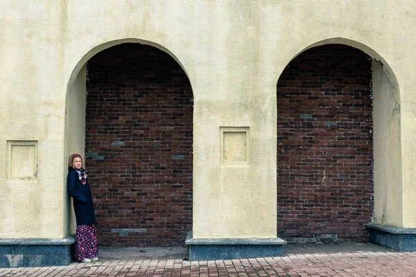 Une femme blonde en manteau noir se tient sous une arche — Photo