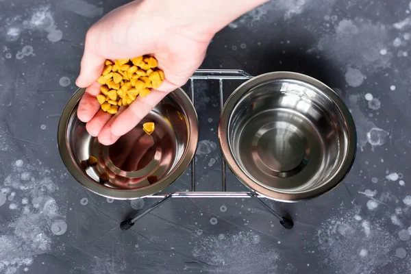 Mão derramando alimentos secos em uma tigela de aço para o gado. Alimentando seu animal de estimação. — Fotografia de Stock