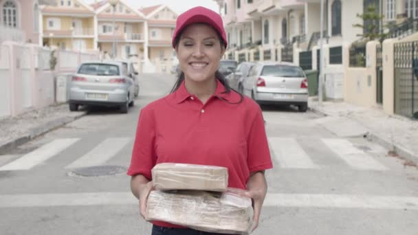 Kırmızı üniformalı mutlu kurye kız elinde paketler tutuyor. — Stok video