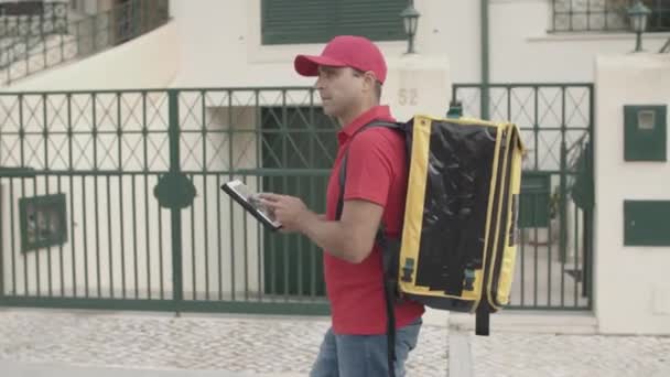 Курьер с термальным рюкзаком и планшетом доставляет еду — стоковое видео