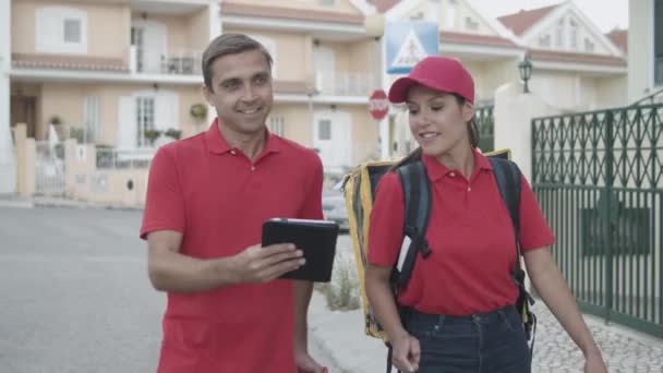 Två glada kurirer i röda uniformer går utanför — Stockvideo