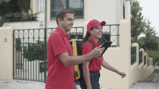 Два веселых курьера в красной форме выходят на улицу. — стоковое видео