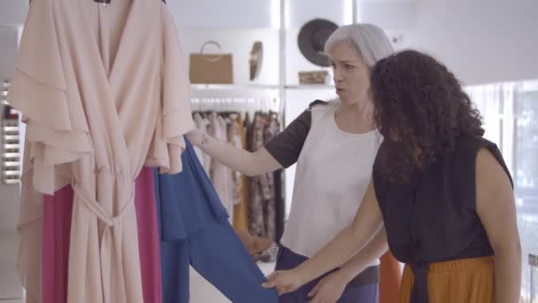 Amigos femininos positivos escolhendo roupas na loja de moda — Vídeo de Stock