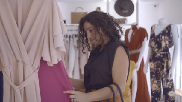 Pensive vrouwelijke klant browsen kleding in de winkel — Stockvideo