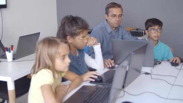 Computer science leraar zit aan een bureau in de buurt van kinderen — Stockvideo