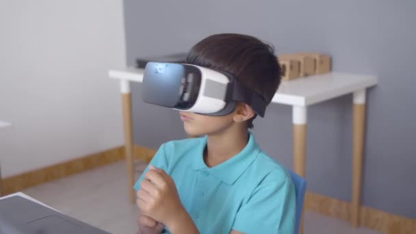 Écolier portant des lunettes VR assis au bureau — Video