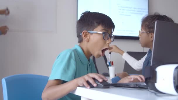 坐在桌旁，使用笔记本电脑的戴眼镜的兴奋的小学生 — 图库视频影像