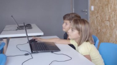 İki sınıf arkadaşı dizüstü bilgisayarlarıyla masada oturuyor.