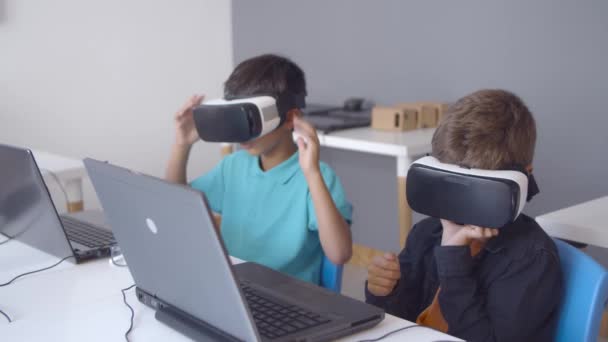 Schoolboys vestindo fone de ouvido VR sentado na mesa com laptop — Vídeo de Stock