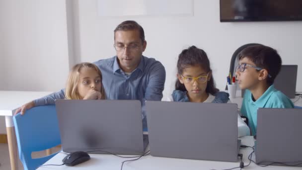 School leraar zit aan een bureau in de buurt van een groep kinderen — Stockvideo