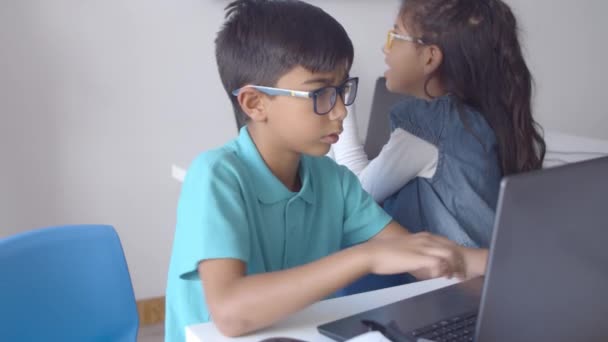 Vážný školní chlapec v brýlích sedí u stolů — Stock video