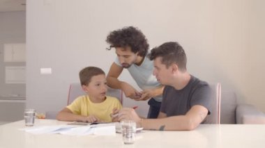İki baba okula odaklanmış çocuğa ev ödevinde yardım ediyor.