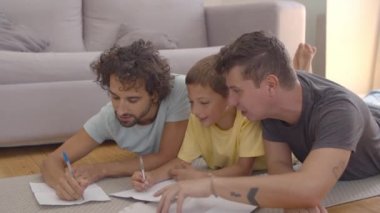 Neşeli babalar ve oğullar yerde yatıyor ve kağıtları çiziyor.