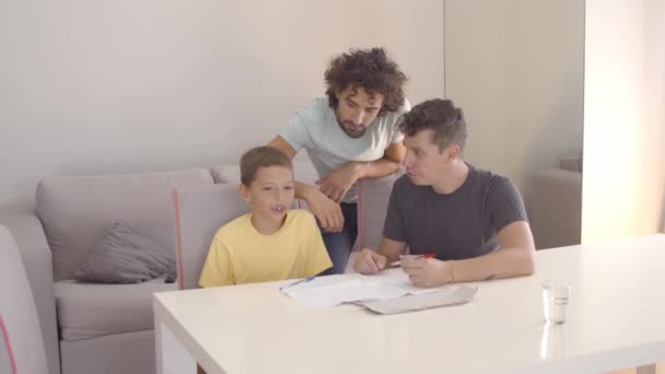 Homosexuella föräldrar hjälper sin son med skrivuppgiften — Stockvideo