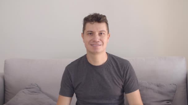 Glücklicher gutaussehender Mann in lässigem T-Shirt auf Couch sitzend — Stockvideo