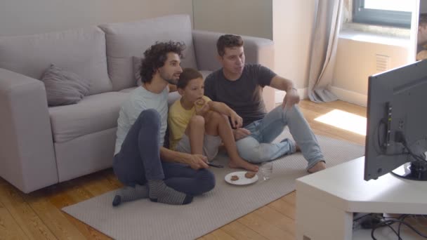 Konzentrierter Junge und seine Väter essen Kekse und schauen Film — Stockvideo