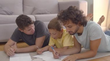 Odaklanmış rahatlamış baba ve oğul yerde yatıyor ve çizim yapıyor.