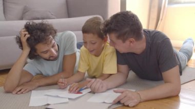 İki baba, odaklanmış çocuğa ev işlerinde yardım ediyor.