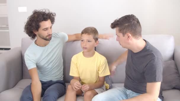 Töprengő fiú ül a kanapén a két apjával. — Stock videók