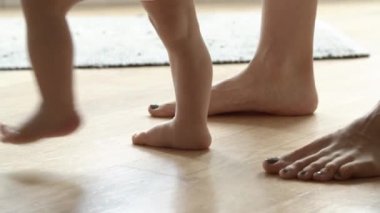 Yalınayak çocuk öğreniyor. Annesinin yardımıyla yerde yürüyor.