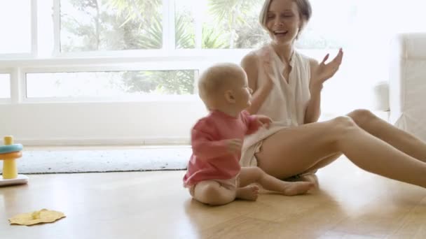 Boldog anya fogja a kezét, játszik a babával, és ül a földön — Stock videók