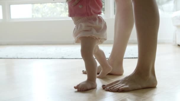 Bonito bebê descalço aprendendo a andar com a ajuda da mãe no chão — Vídeo de Stock