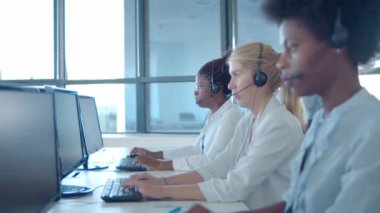 Erkek çağrı merkezi yöneticisi kulaklıklar içinde operatörlerin yanında.