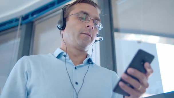Skupiony operator męski w słuchawkach przewodowych z telefonem komórkowym — Wideo stockowe