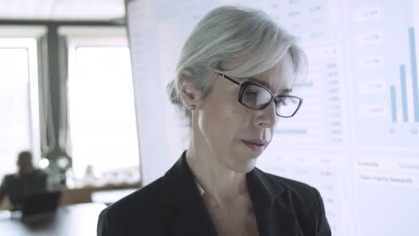 Femme d'affaires aux cheveux gris en lunettes tenant la tablette et tapant — Video