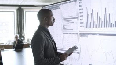 Tablet kullanan, ayakta duran konsantre olmuş melez iş adamı.