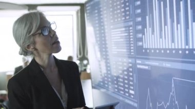 Tablet kullanan ve ayakta duran orta yaşlı bir iş kadını.