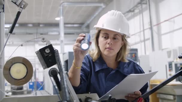 초점을 맞춘 여성 기술자가 손전등으로 기계를 조사하는 모습 — 비디오