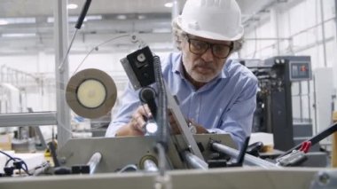 El feneriyle makineyi incelemeye odaklanmış eski fabrika mühendisi