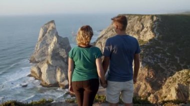 Romantik çift el ele tutuşuyor, kayalık kayalıklarda duruyor.