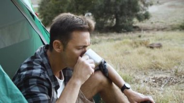 Düşünceli kampçı sıcak çay ya da metal bardaktan kahve içiyor.