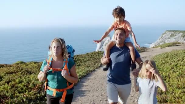 Happy couple of parents and children walking on path at sea — Stock Video