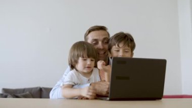 Orta yaşlı baba oğullarına sarılıyor ve online oyun oynuyor.