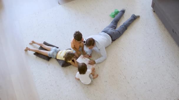 Grand angle de frères et sœurs enfants et papa assis et couché sur le sol — Video