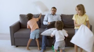 Orta yaşlı baba çocuklarla oynuyor ve yastıklarla kavga ediyor.