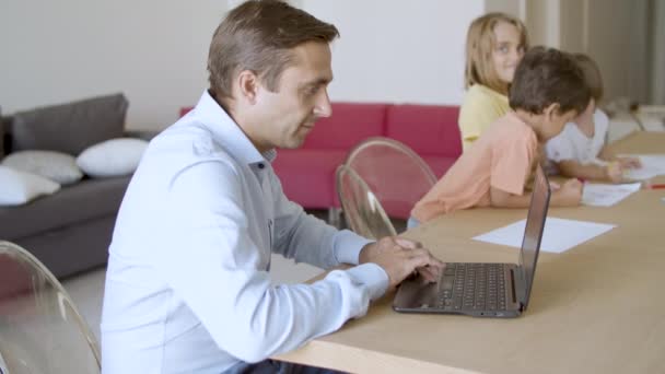 Valkoihoinen isä työskentelee kannettavan tietokoneen ja söpö lapset maalaus doodles — kuvapankkivideo