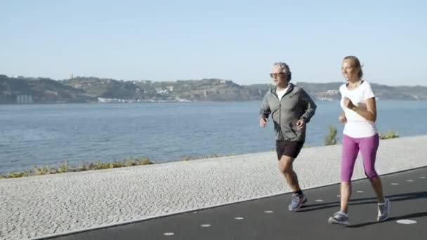 Active man and woman jogging on asphalt road along sea — Stock Video