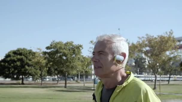 Active old jogger with headphones running outside — Αρχείο Βίντεο