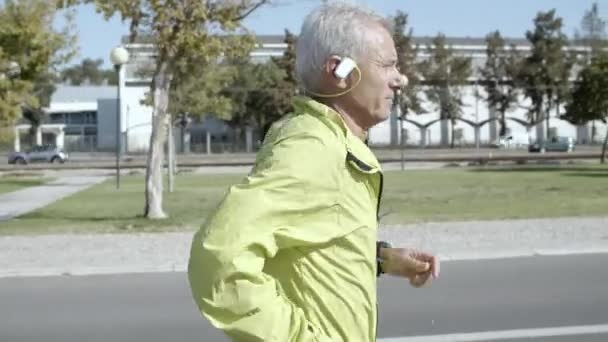 Pensionato maschio attivo con apparecchio acustico che fa jogging all'esterno — Video Stock