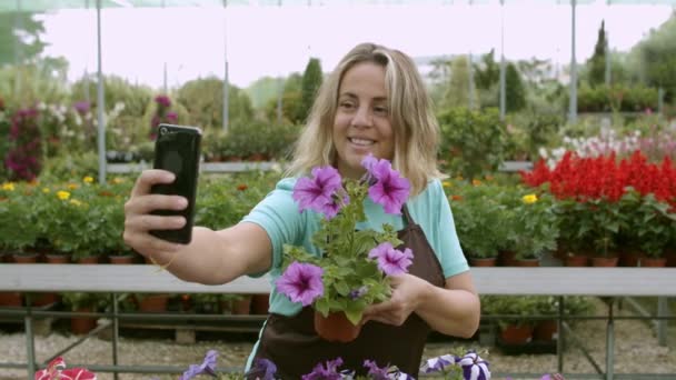 Szczęśliwy kobieta kwiaciarnia gospodarstwa doniczkowy kwiat i biorąc selfie — Wideo stockowe