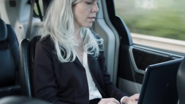 Žena sedí na zadním sedadle jedoucího auta, píše na notebook. — Stock video