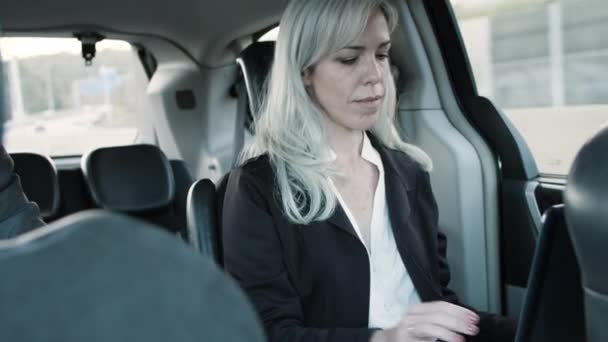 Gray-haired zakenvrouw rijden in de auto en het inschakelen van laptop. — Stockvideo