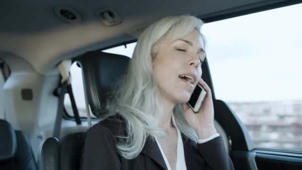 Gråhårig affärskvinna pratar i telefon medan du kör bil. — Stockvideo