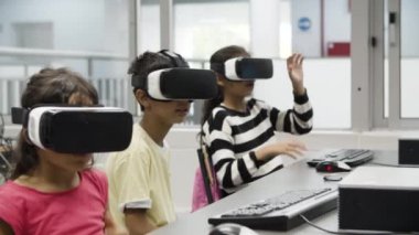 Çok ırklı çocuklar VR kulaklık takıyor ve masada oturuyorlar.. 