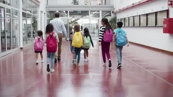 Vue arrière des enfants marchant avec un tuteur masculin dans le couloir de l'école. — Video