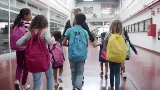 Мультиэтнические дети идут по коридору с учительницей — стоковое видео